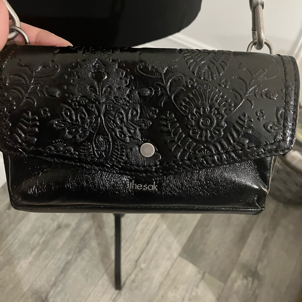 The Sak black small crossbody bag with embossed floral design and woven strap.